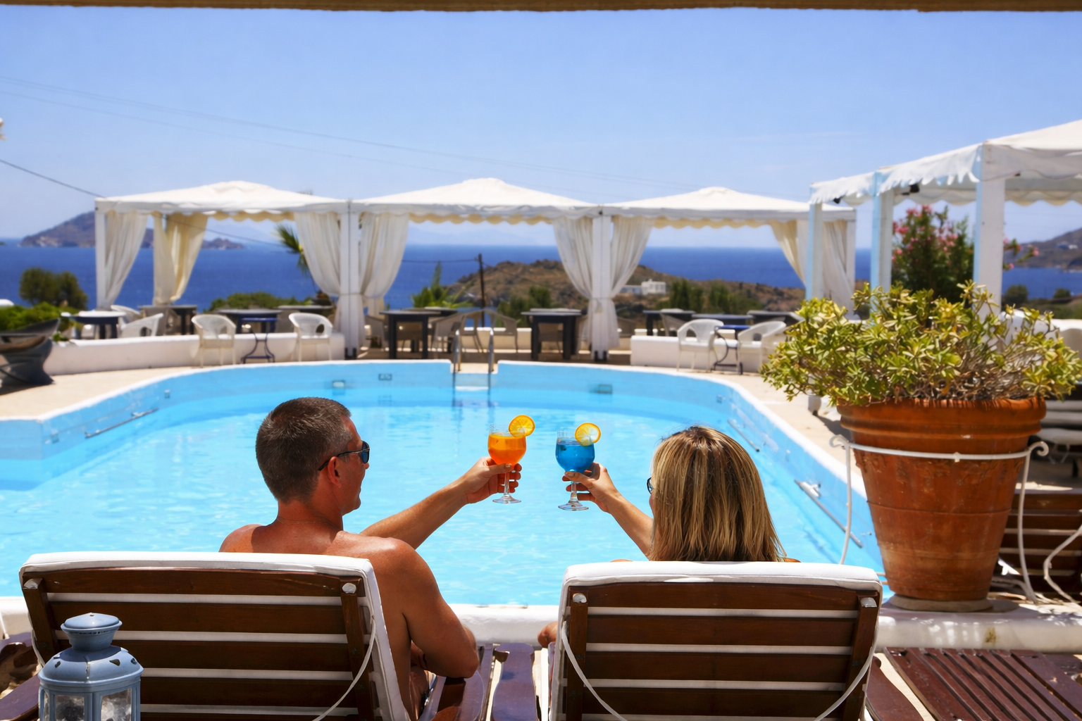 Couple toasting cocktails by the pool with sea view